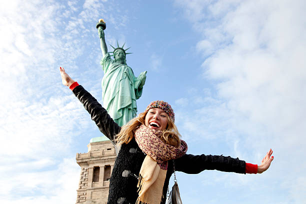 a beautiful young blonde woman at the statue of liberty in new york.